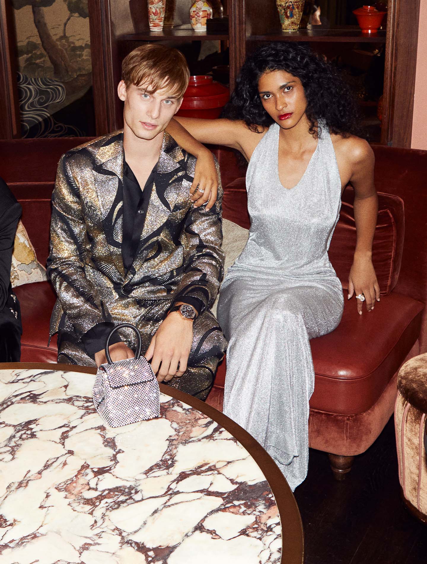 Man and woman sitting on sofa, women in a silver sparkly dress and the man in a metallic patterned suit