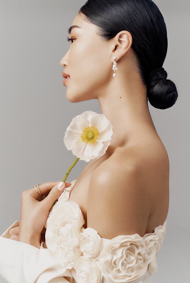 A model wears pearl Sophie Bille Brahe earrings and a cream Anna October dress while holding a flower