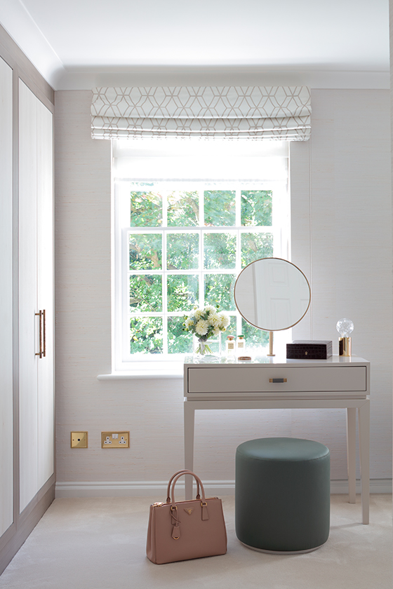 Dressing table in front of large window with a green stool and built in wardrobes