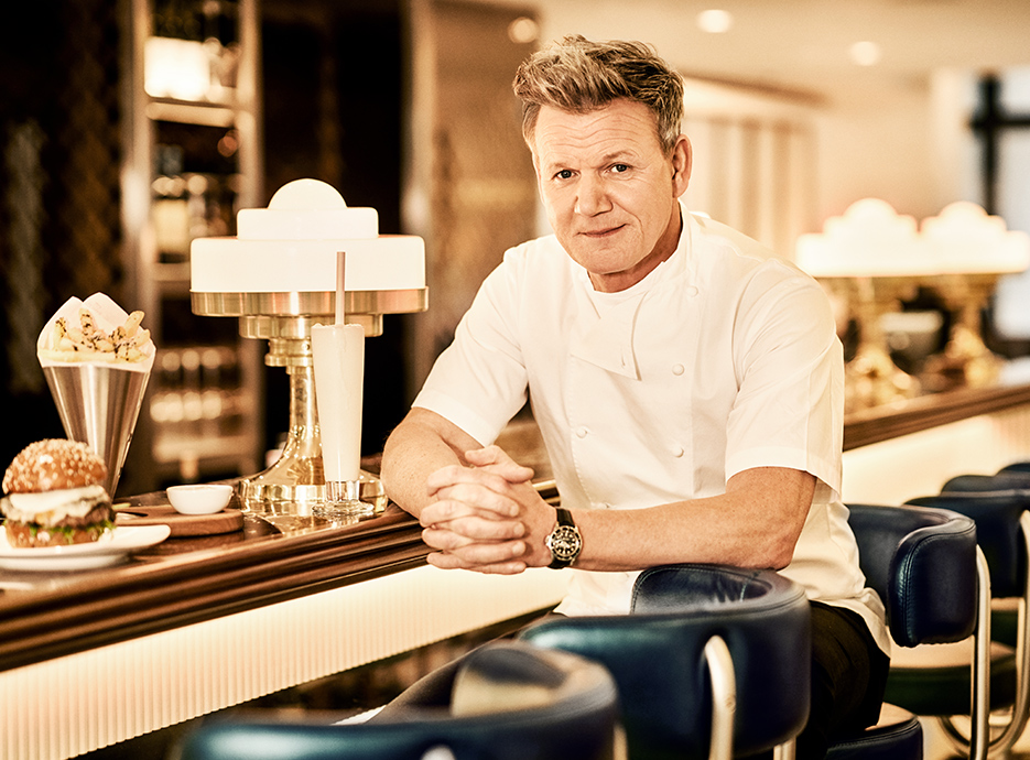 Gordon Ramsay sitting at the bar with burger and fries