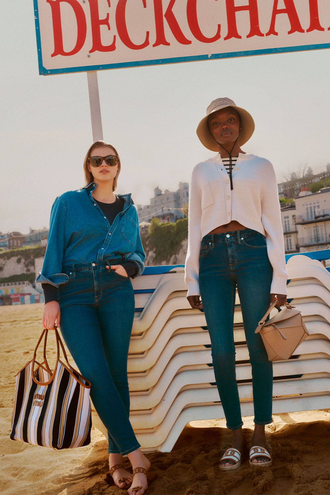 Two models stand in front of deckchairs on British beach and wear casual denim looks with Good American jeans