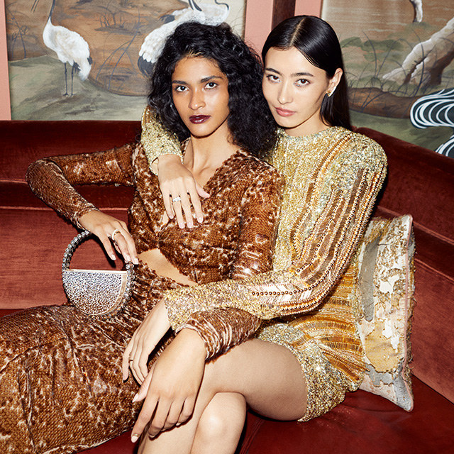 Two women sitting on a sofa at a party in sparkly sequin dresses