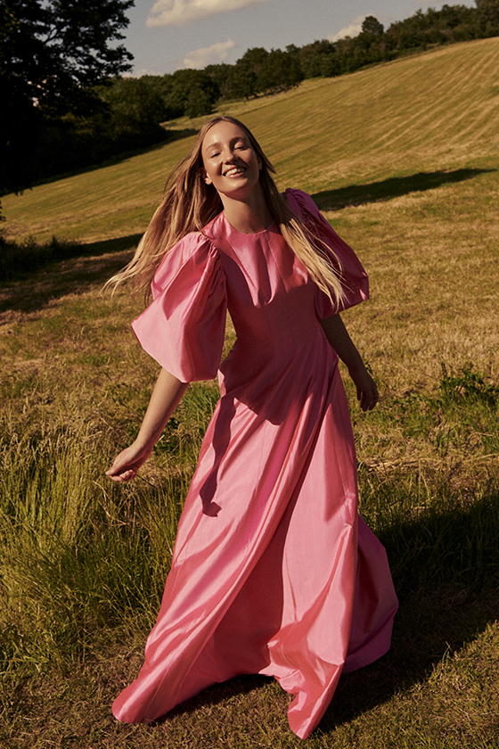 Ellie in pink satin dress standing in a field