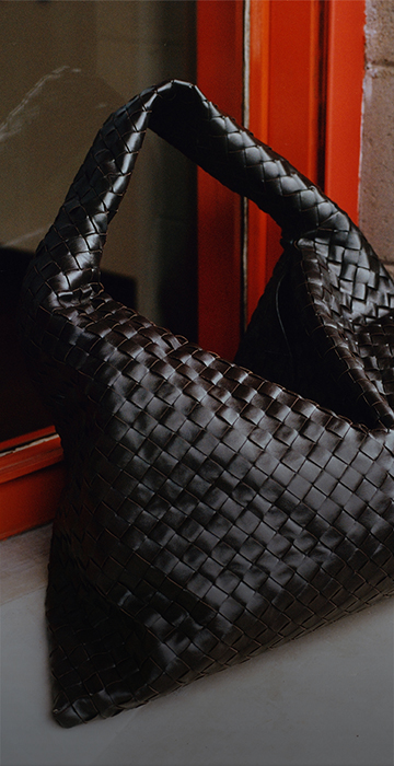 Women holding a white Bottega Veneta woven clutch, and wearing a cream fur coat with gold heart hardwear detailing