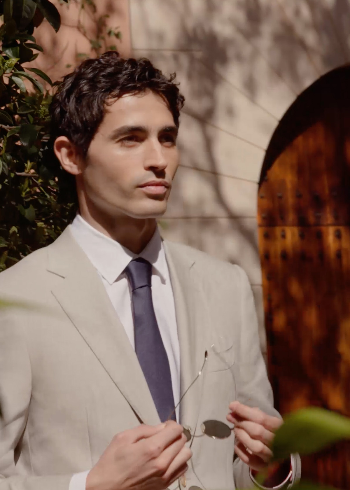 Video of male model wearing beige Canali suit and navy tie standing in sunny location