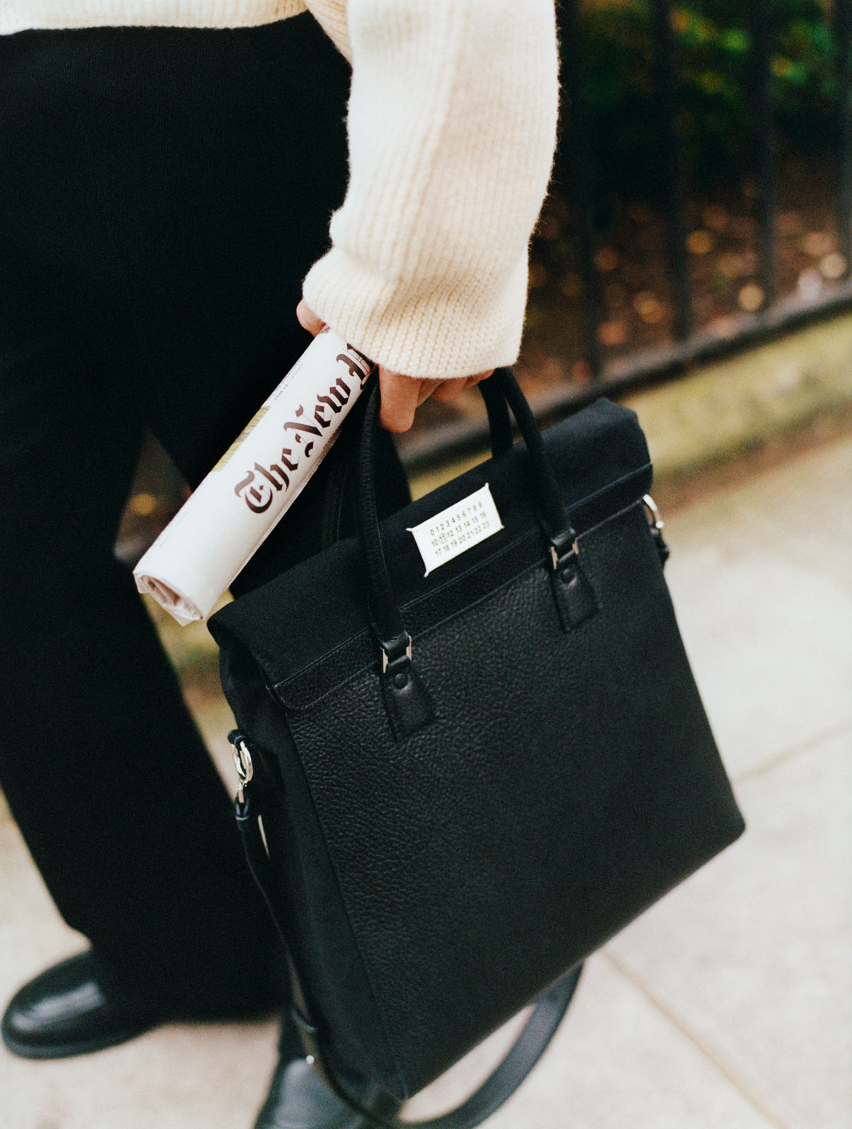 A male model carries a copy of The New York Times and a black leather bag by Maison Margiela