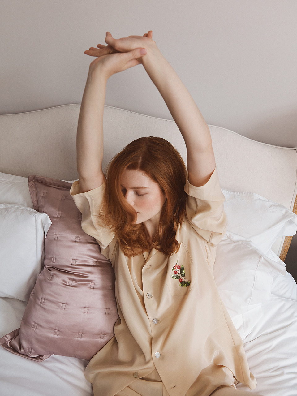 Model sat on bed stretching wearing  Olivia Von Halle yellow pyjama set