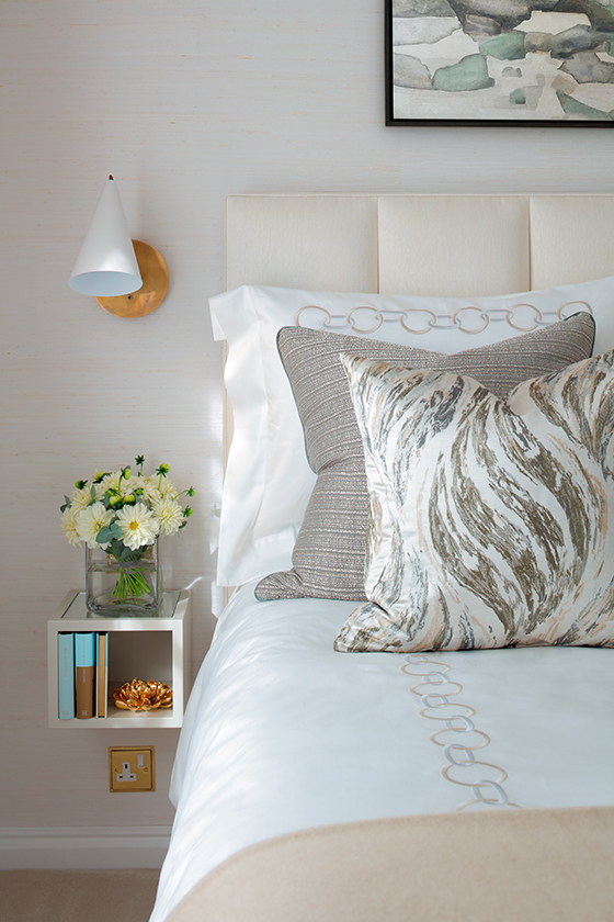 Small square bedside table in master bedroom with gold and white wall lamp