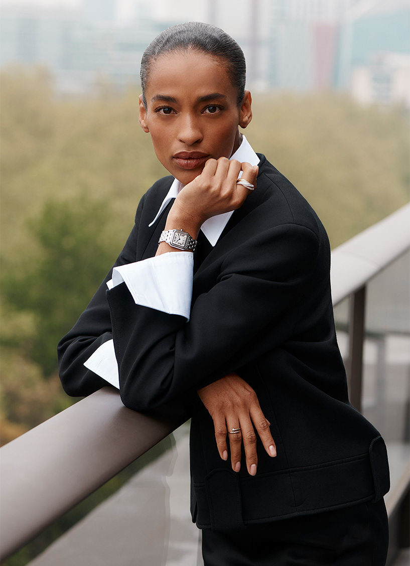 Models wears a white shirt and black suit jacket and a Cartier watch standing on a balcony