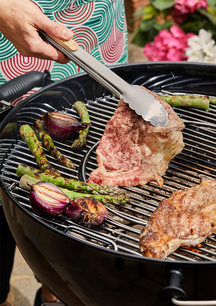 Steak and vegetables grilling on a black BBQ