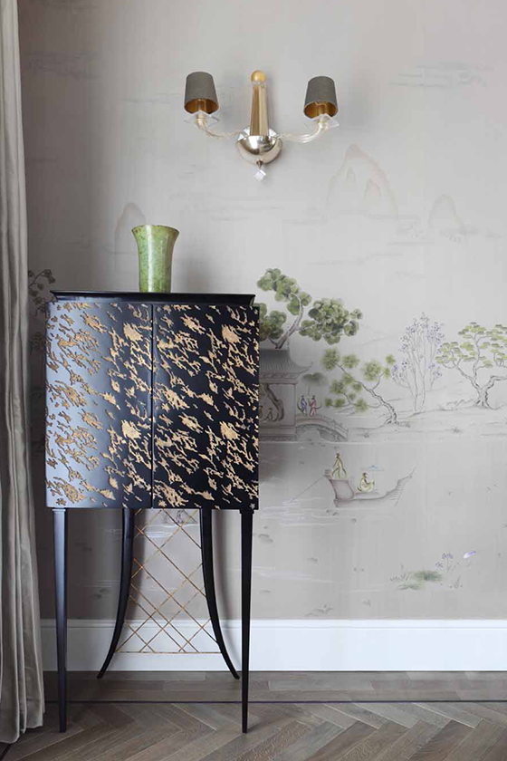 Black wooden carved side table in front of a wall with hand drawn wall paper