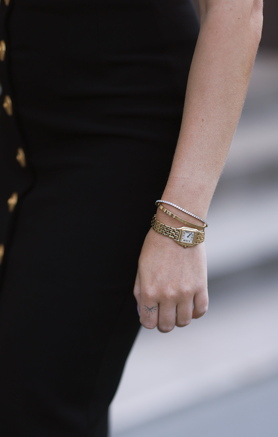 Woman in a black dress with gold button accents wearing a gold Cartier watch and bracelets