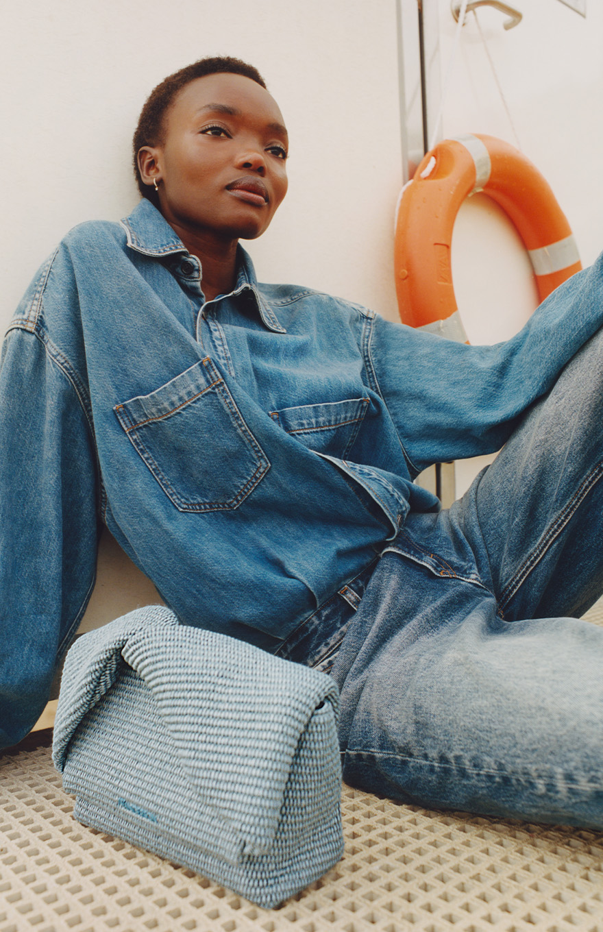 Model sits wears blue denim Haikure jumpsuit