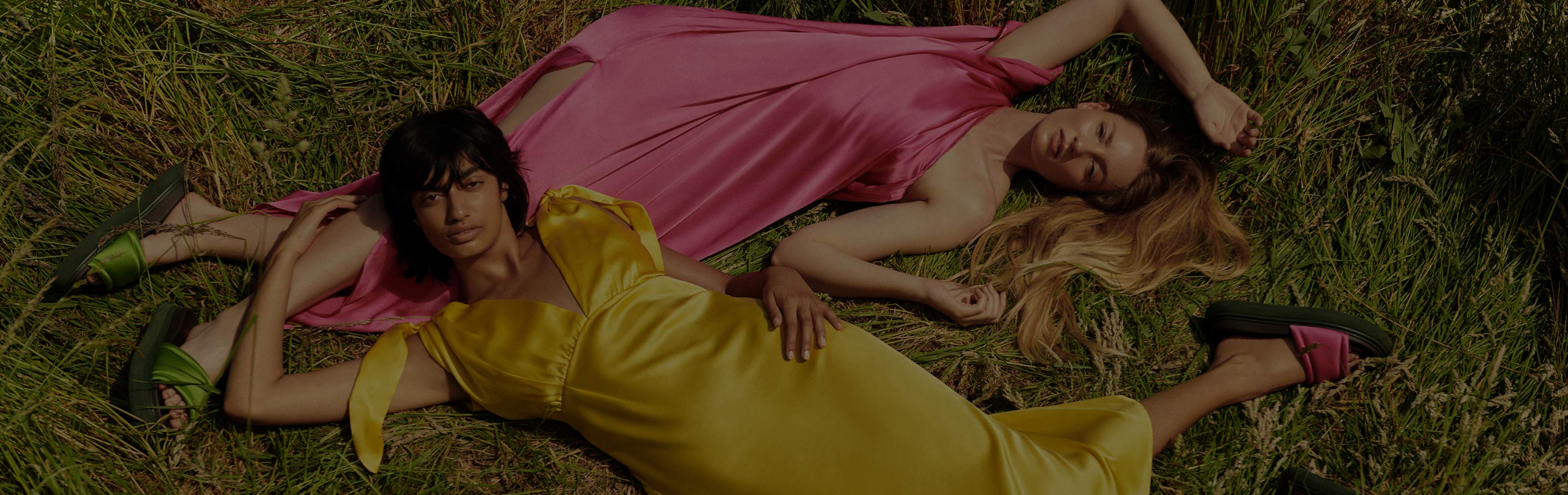 Ellie and Ameera laying on the grass in bright pink and yellow silk dresses