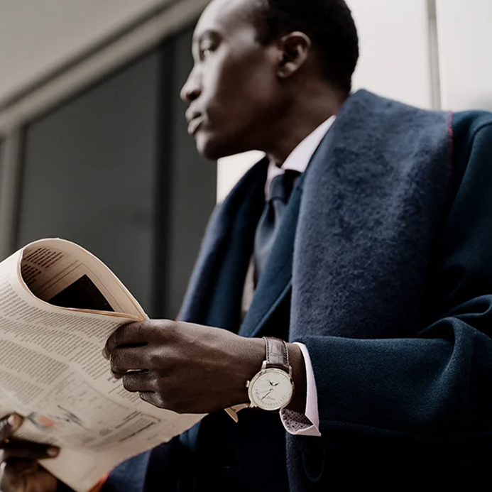 A man wears a smart suit, reads a newspaper and wears a Vacheron Constantin watch