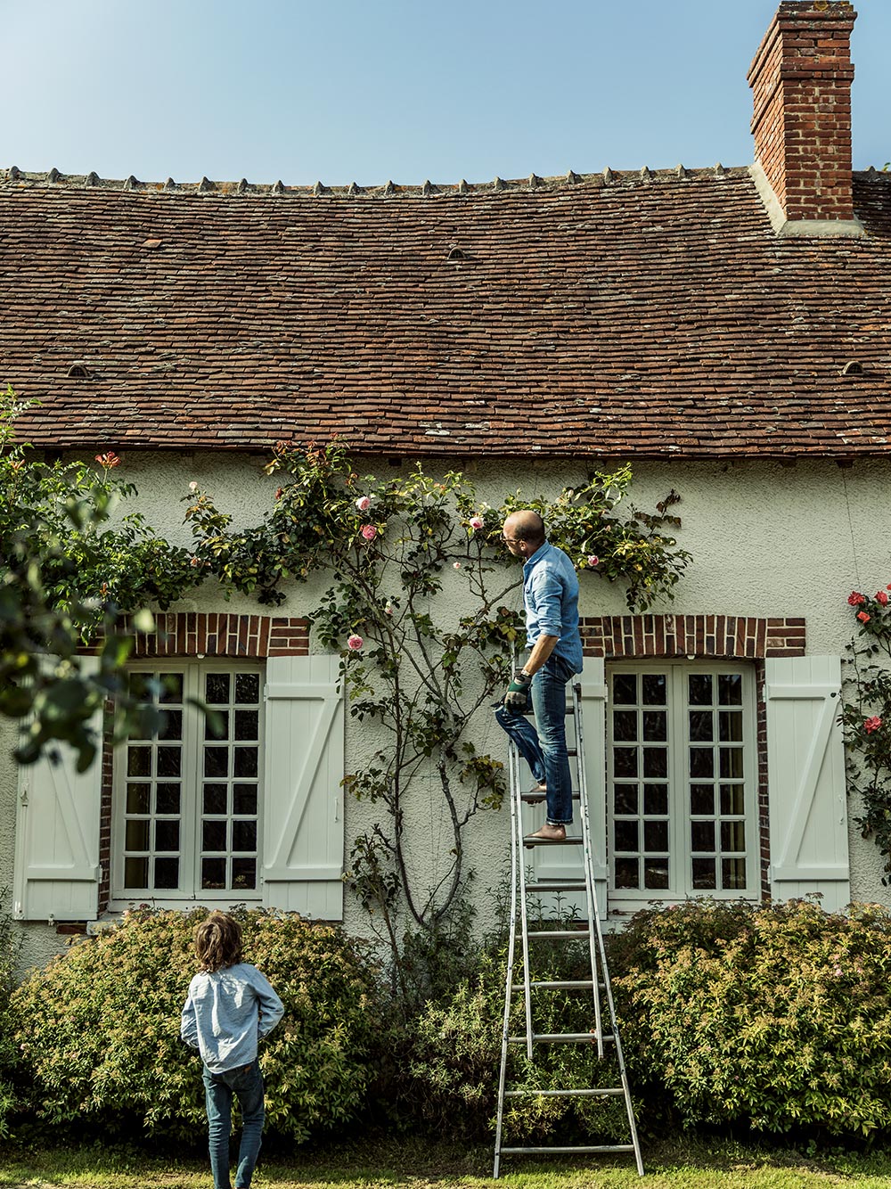 Pierre Prey and his son standing outside his house looking at roses